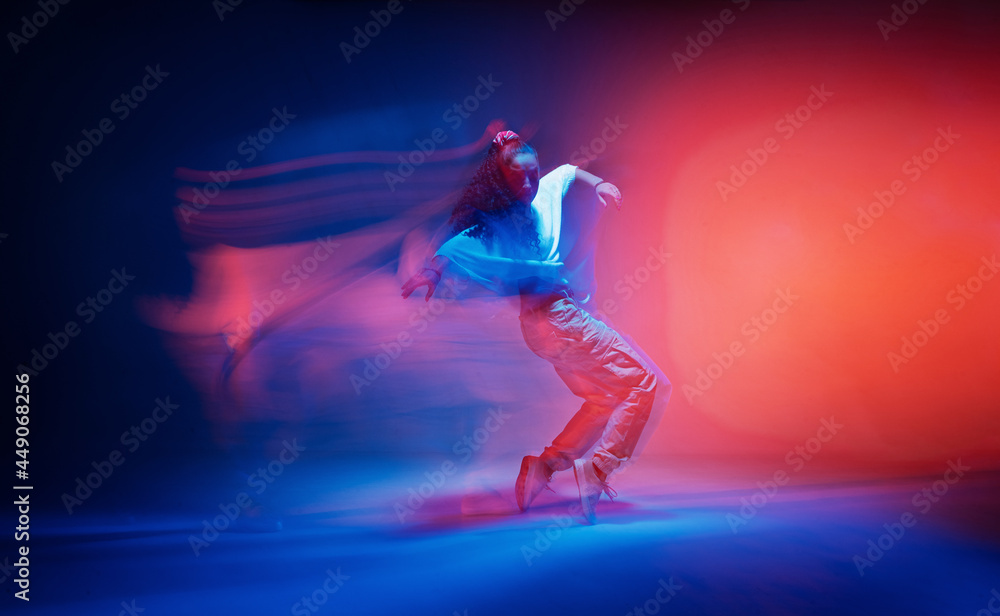 Dancing female standing on tiptoe in colourful neon studio light. Long exposure. Contemporary hip hop dance
