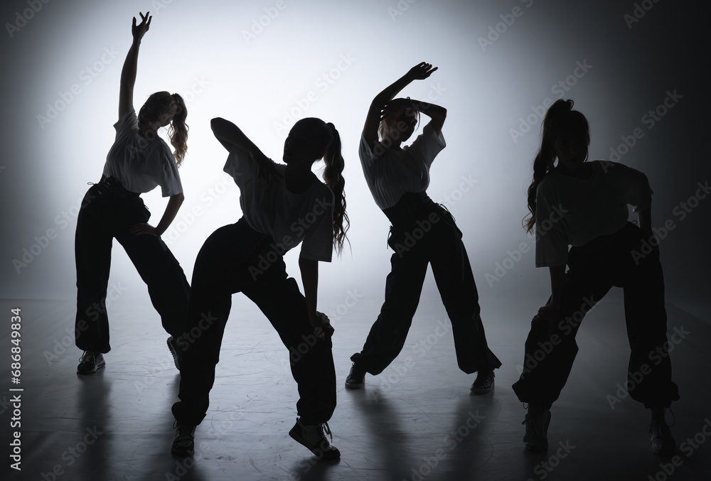 In the shot on a black background in the light of a spotlight in the silhouette. Dance group consisting of attractive girls. They show dance moves towards jazz funk.